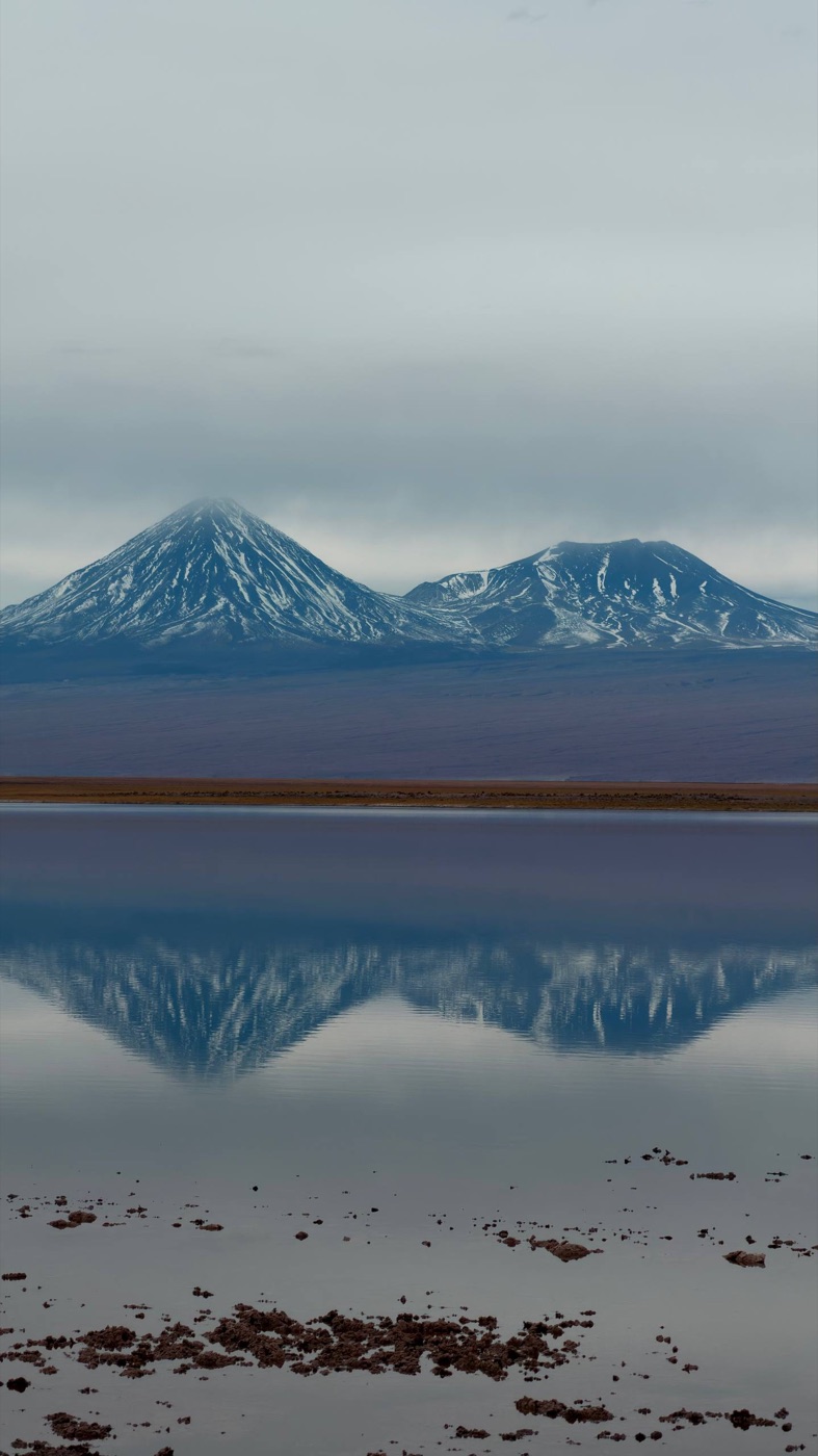 O reflexo perfeito dos vulcões nevados na água parada da Laguna Cejar