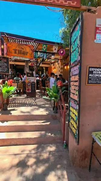 Entrada colorida do Ckunza Tilar em San Pedro de Atacama, com lousas de menu pintadas à mão, plantas e mesas ao ar livre