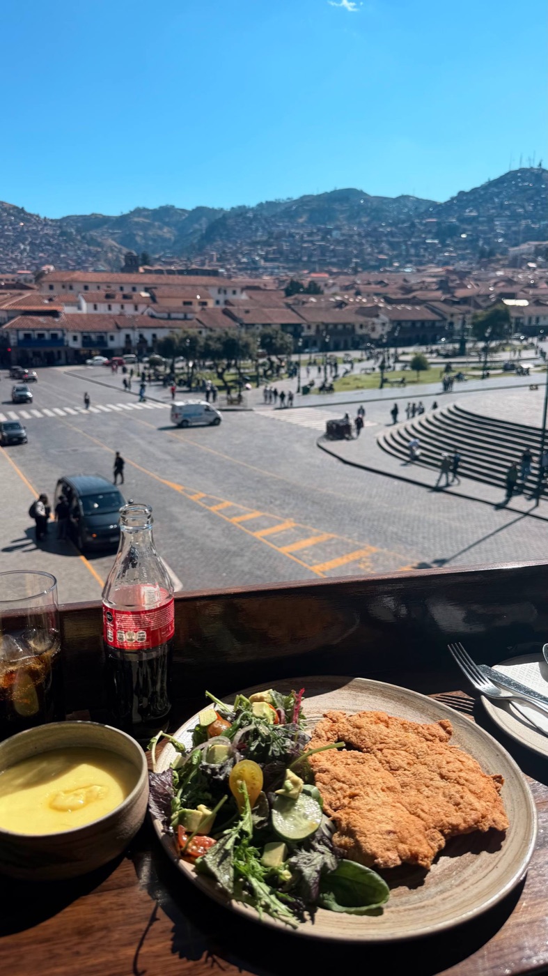 A milanesa com salada e purê na mesa da terraça do Casa Cusqueña, com a Plaza de Armas de Cusco e os morros ao fundo