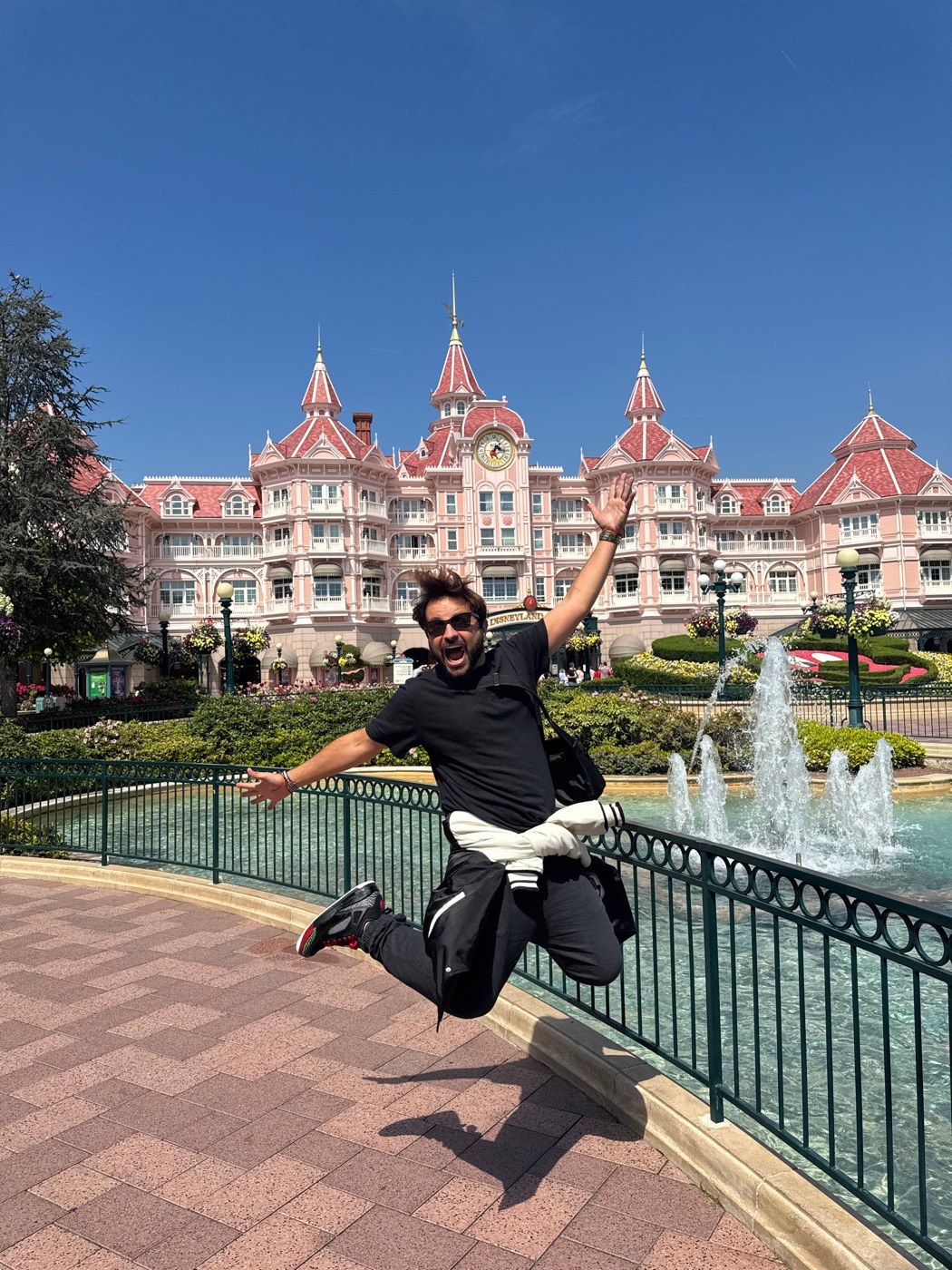 O Dan pulando de braços abertos em frente ao hotel rosa da Disneyland Paris