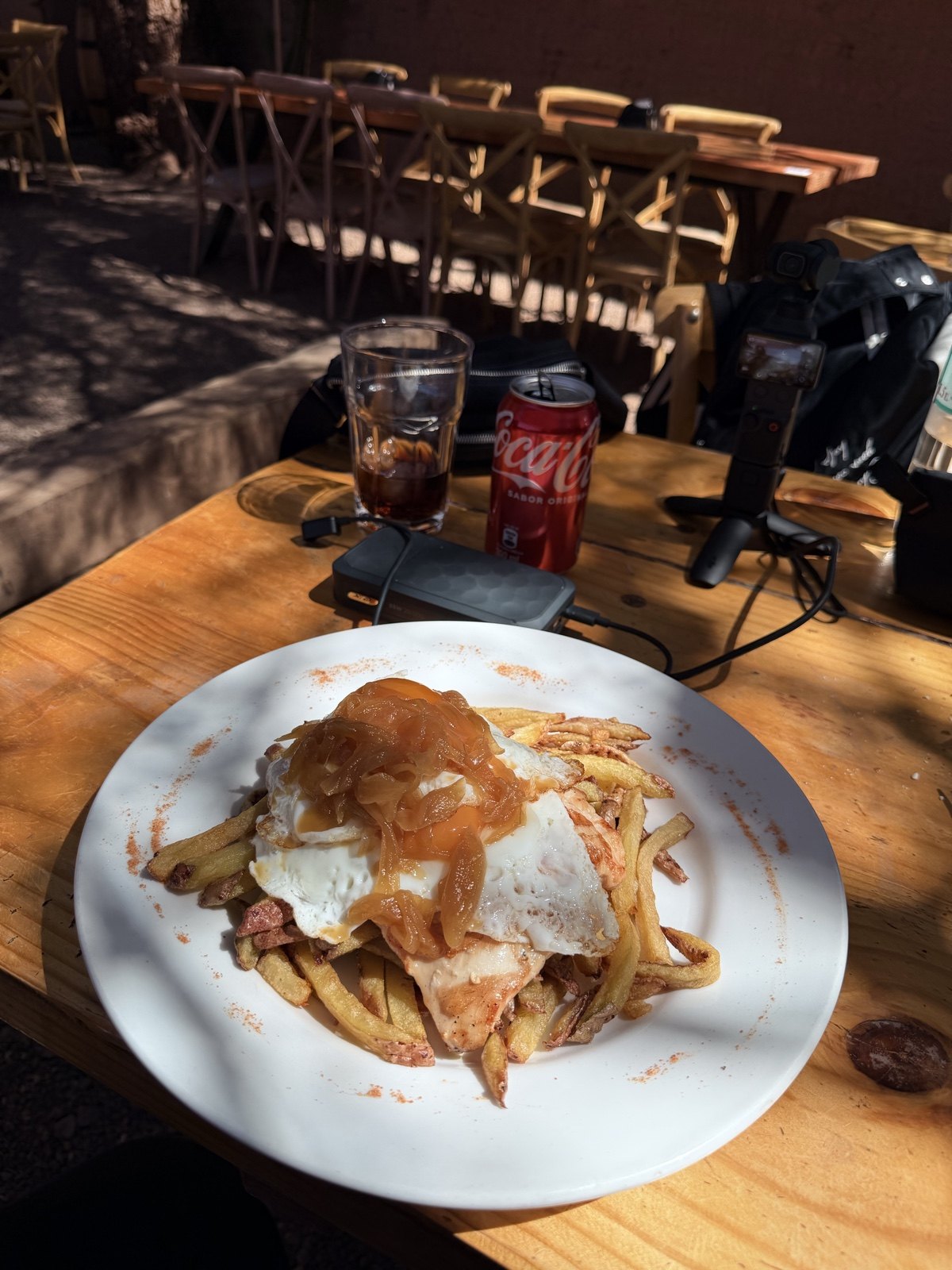 O pollo a lo pobre que o Dan comeu no La Casona em San Pedro de Atacama: frango, batata frita, ovo frito e cebola caramelizada, na mesa de madeira do pátio