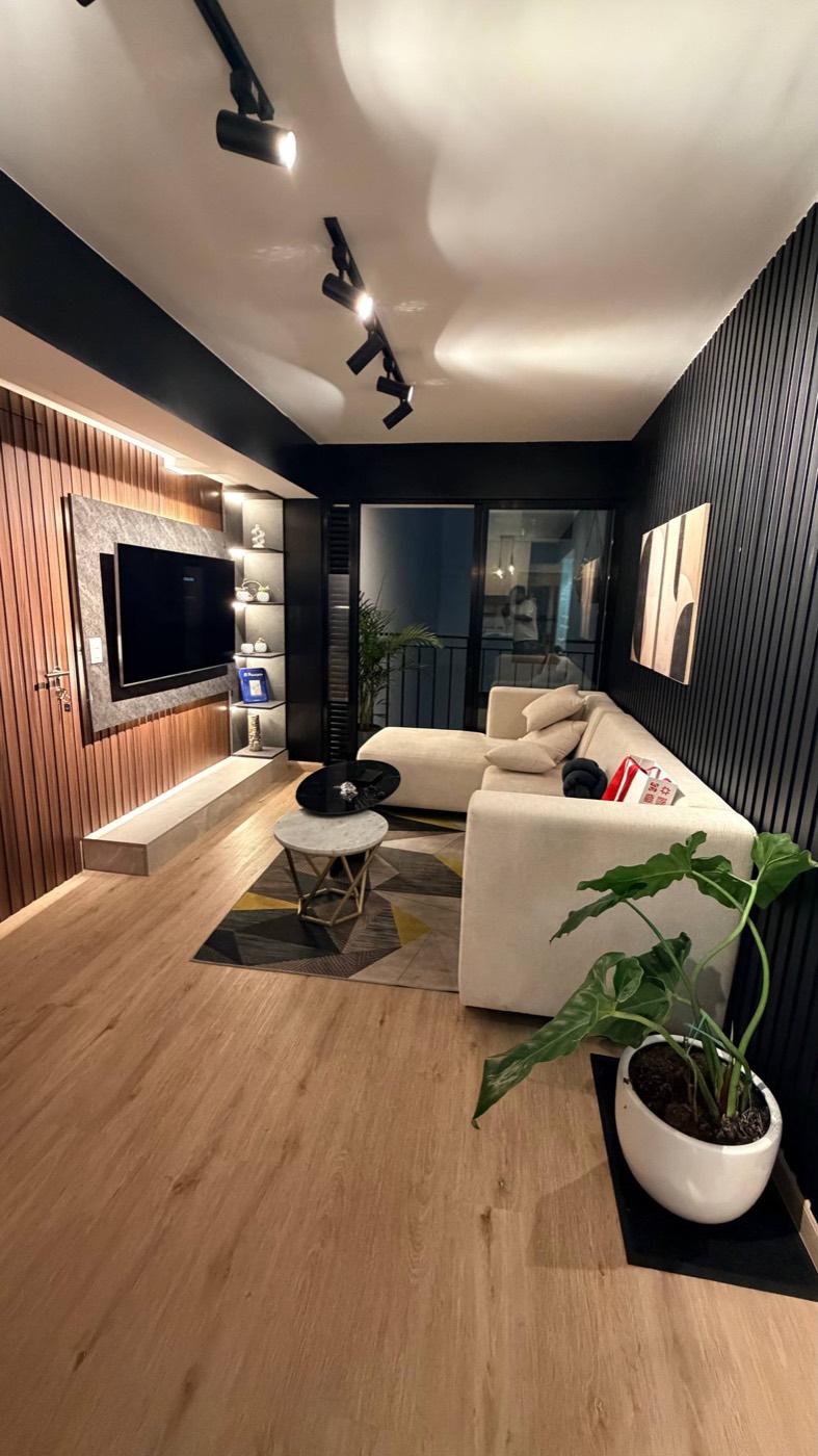 Sala do Airbnb em Miraflores: sofá bege em L, tapete geométrico, mesa de centro de mármore, painel de madeira com TV, parede ripada preta, plantas e a varanda de vidro ao fundo