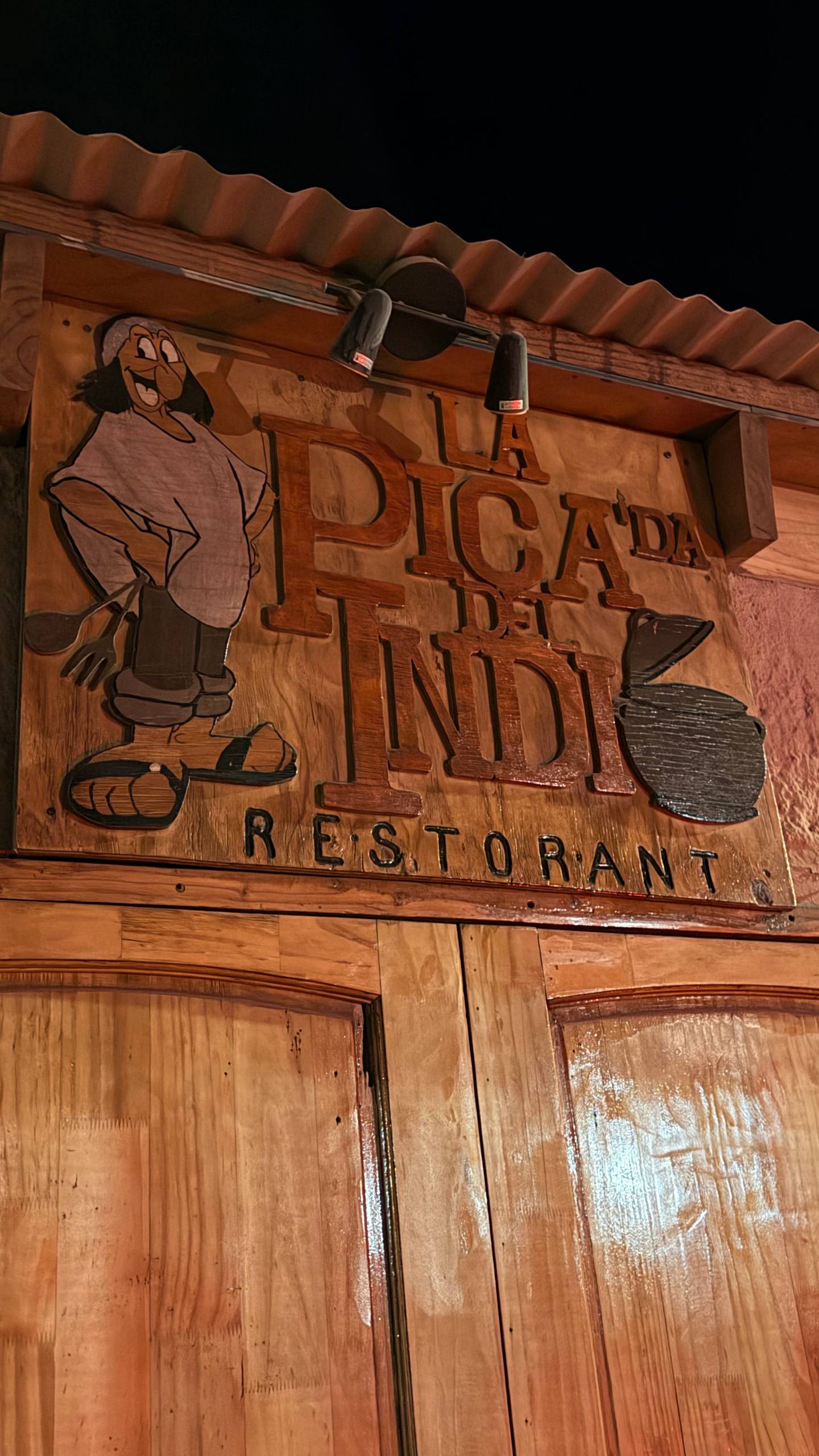 Fachada de adobe do La Pica del Indio em San Pedro de Atacama, com lousas de menu dos dois lados da porta e gente jantando dentro