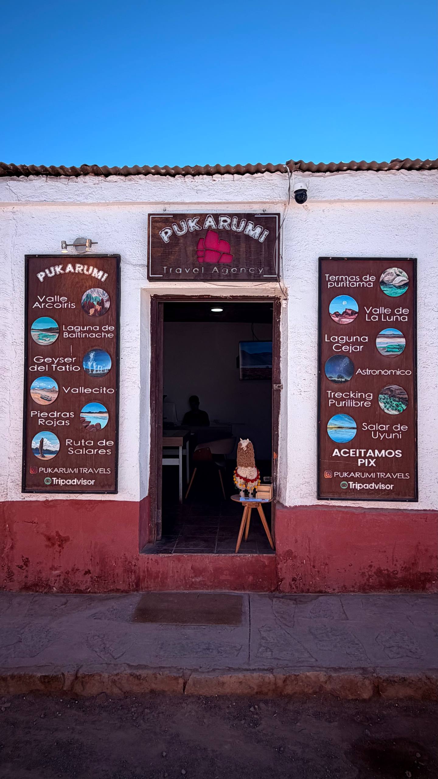 Fachada da agência Pukarumi Travel Agency em San Pedro de Atacama, com as placas de passeios e 'Aceitamos Pix'